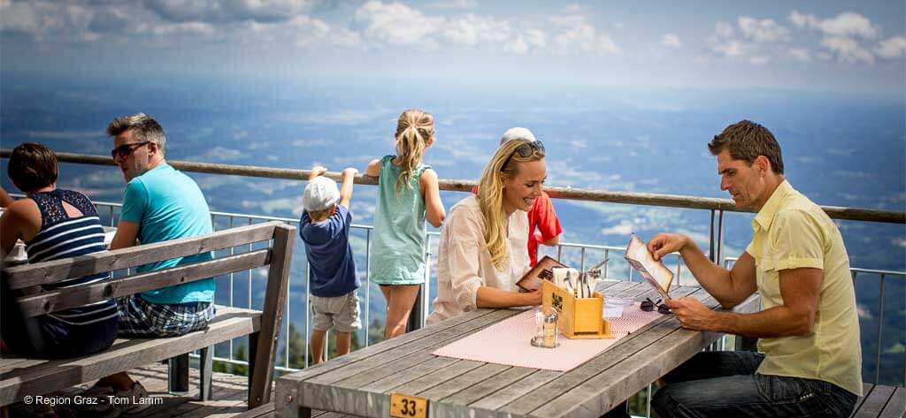 Gäste auf einer Terrasse am Schöckl, die den Blick über Graz genießen